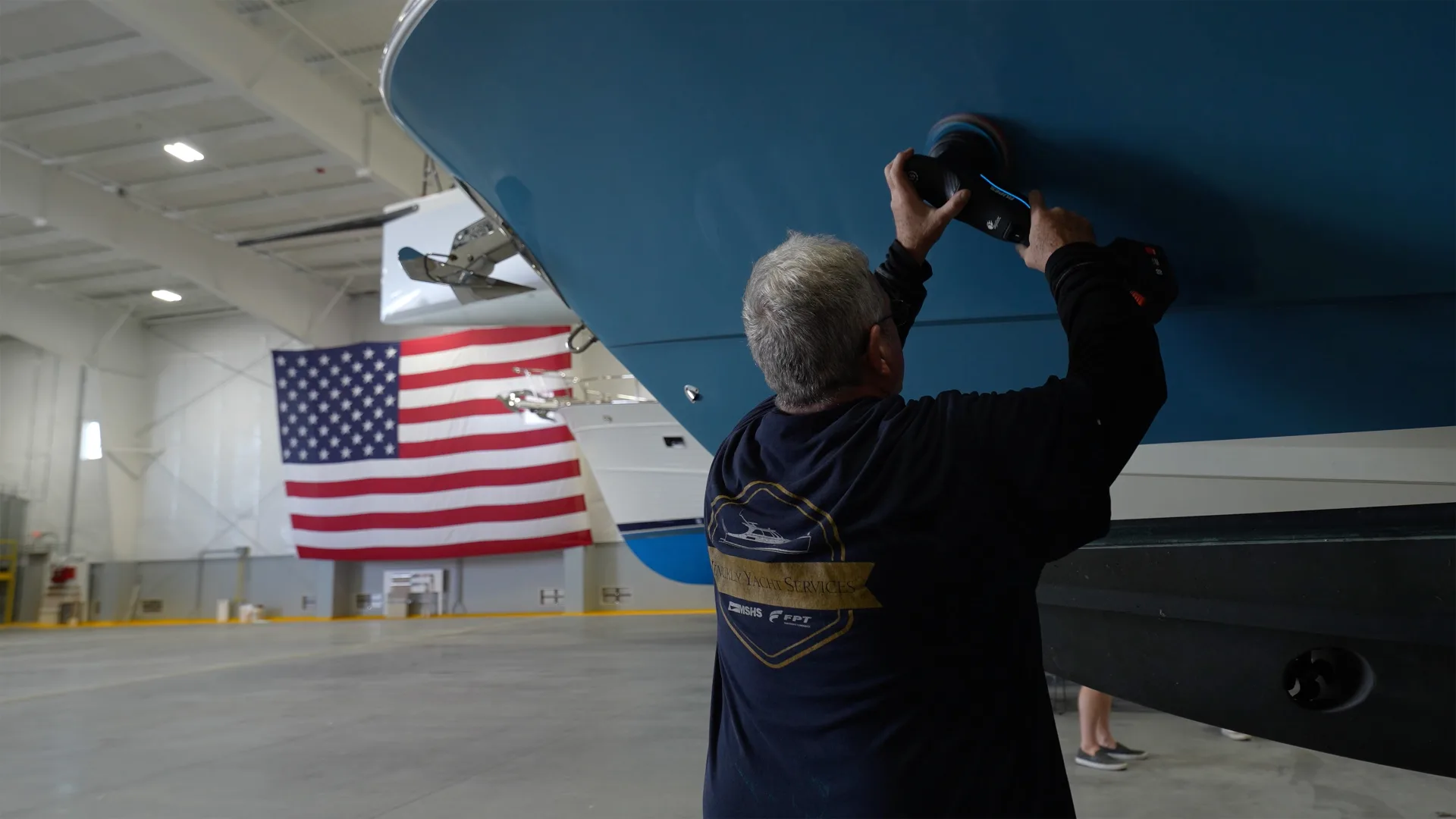 Technician working beneath a raised yacht hull in the Portsmouth service bay