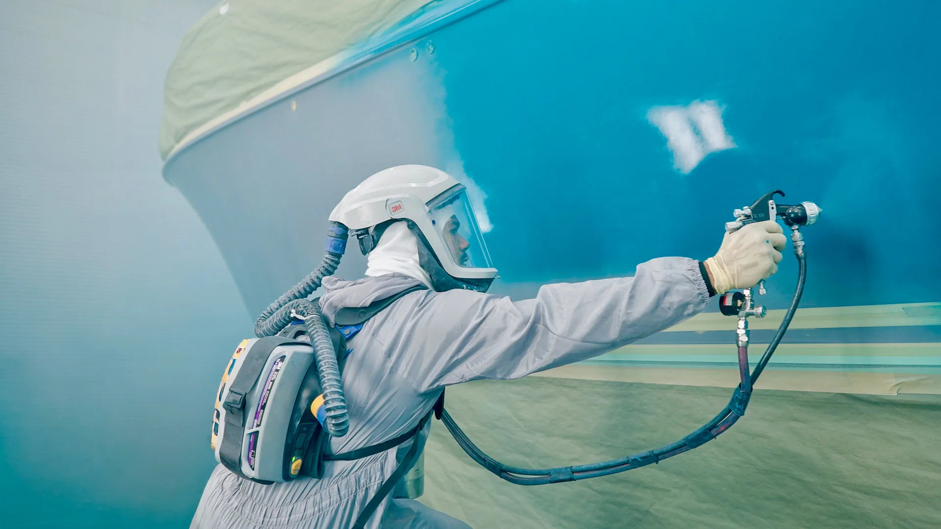 Technician spraying finish onto a blue hull in Stamford