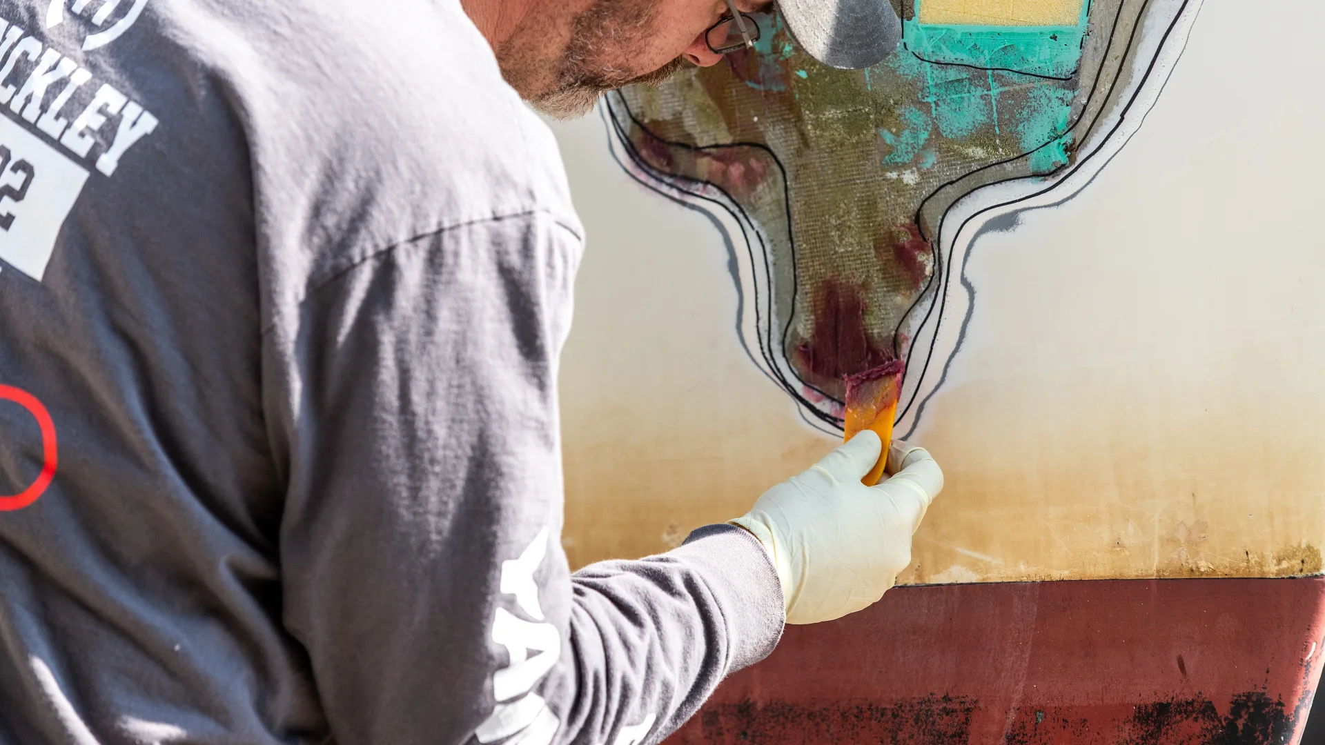 Technician refinishing varnish on a dark yacht hull in Southwest Harbor