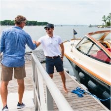 Two people greeting each other on a dock beside a Hinckley boat.