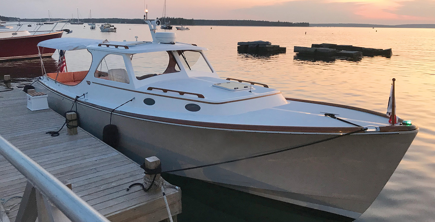 Hinckley motor yacht tied to a dock at sunset, viewed from the bow with calm harbor waters in the background.
