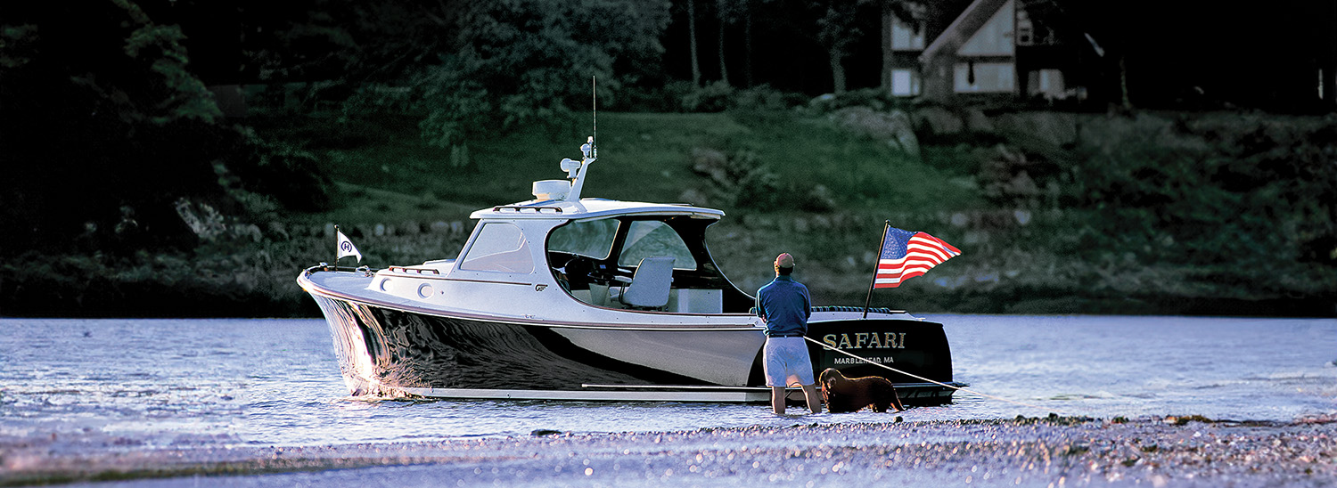 Hinckley motor yacht in shallow water with a person standing at the stern and an American flag flying.