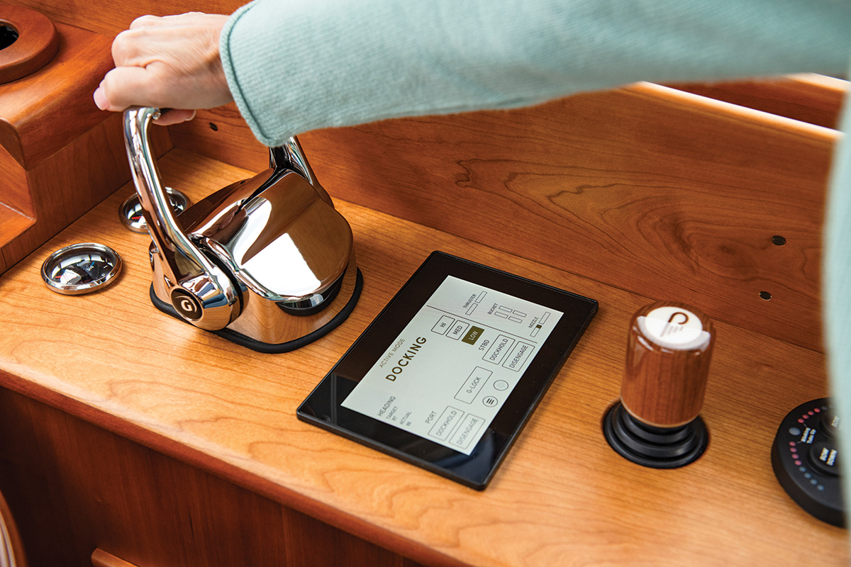 Hand operating a Hinckley JetStick control at a wooden helm with a docking display screen.