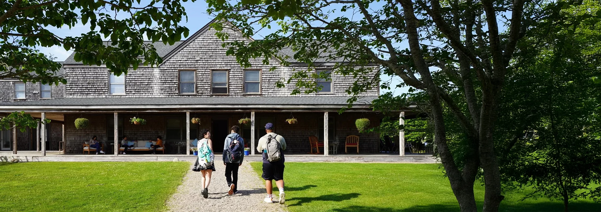 Three people walking toward a historic shingle-style building across a green lawn on Nantucket.