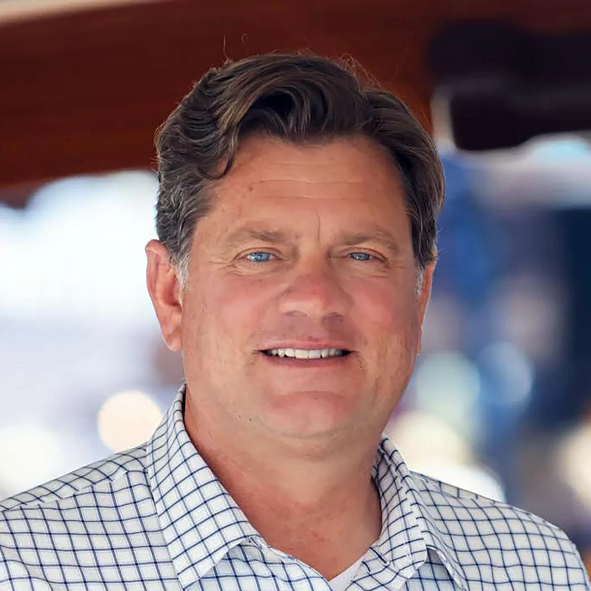 Portrait of a Hinckley Yachts sales consultant wearing a checkered shirt, photographed onboard with a softly blurred marina background.