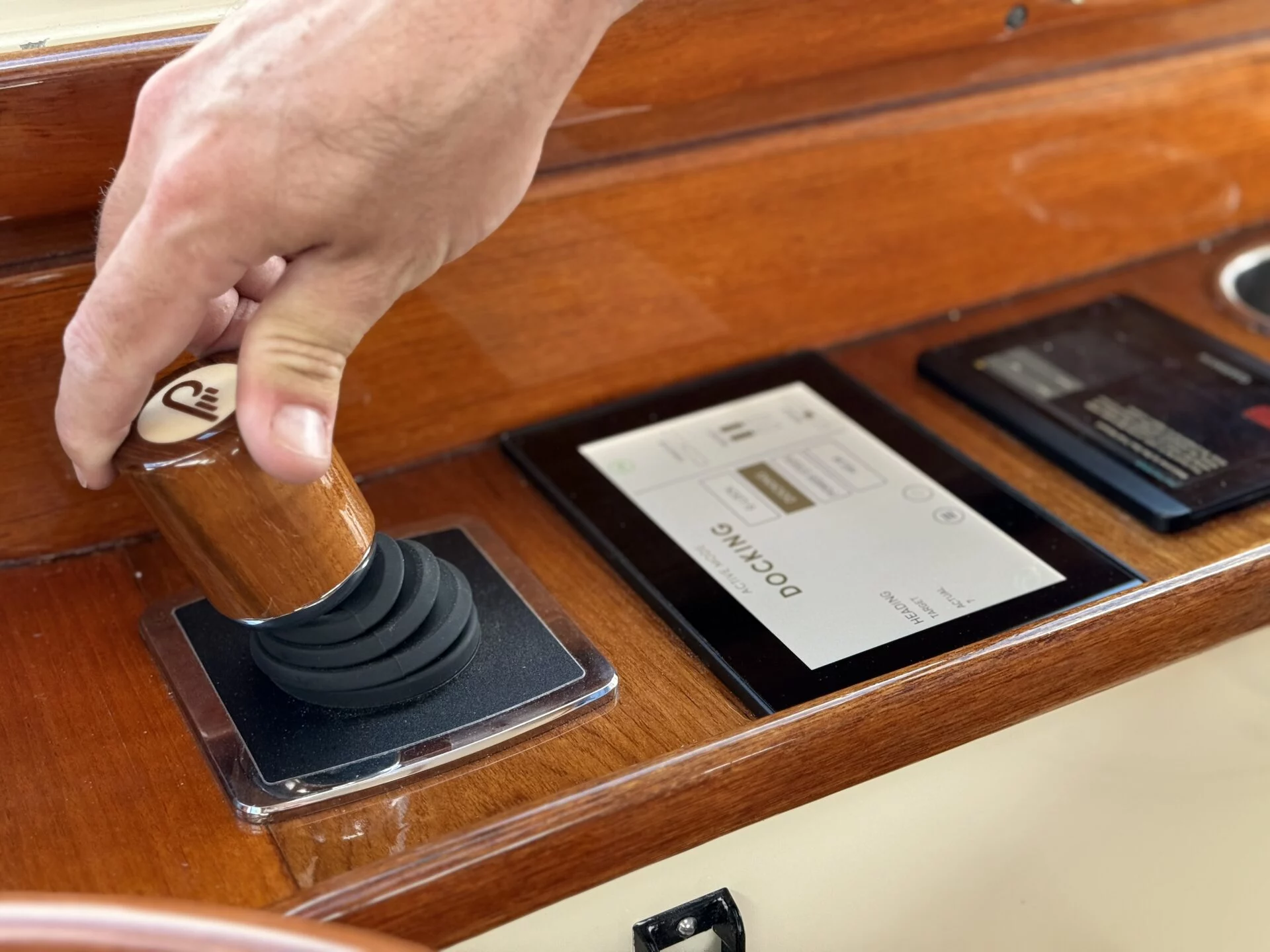 Hand operating the JetStick 3 joystick on the Hinckley Picnic Boat EP, set into a varnished wood helm.