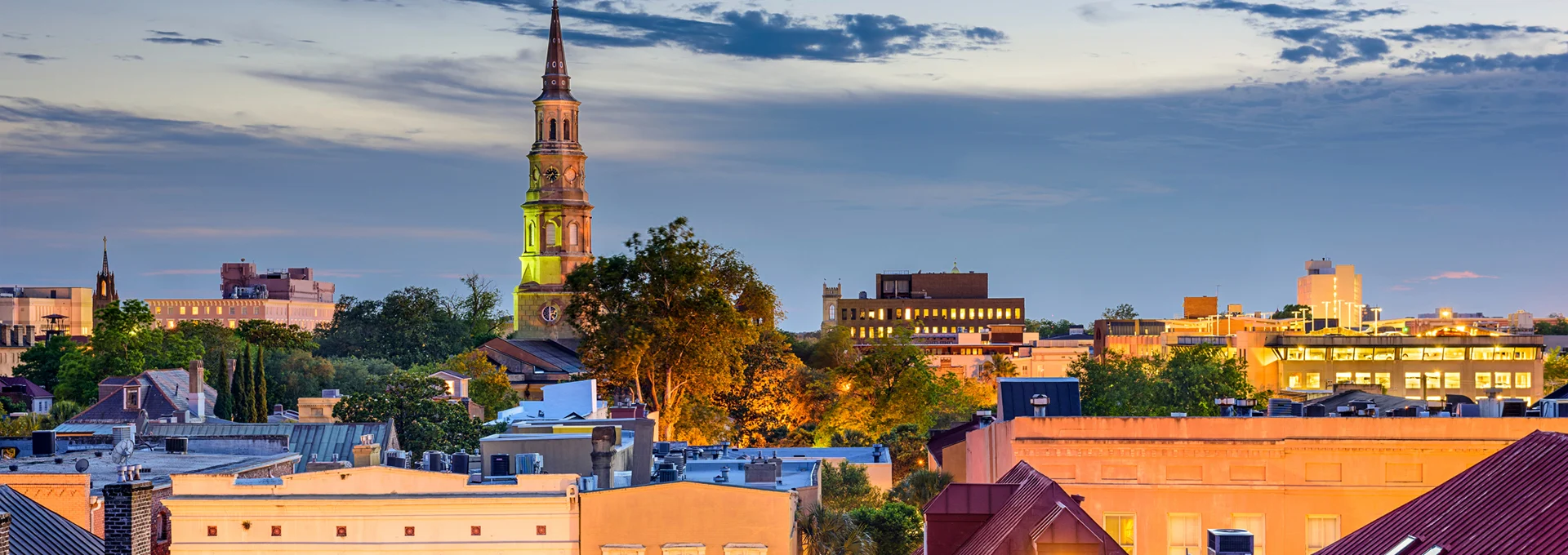 Charleston, South Carolina skyline at dusk featuring historic church steeples and illuminated buildings near Hinckley Yachts’ Charleston office location.