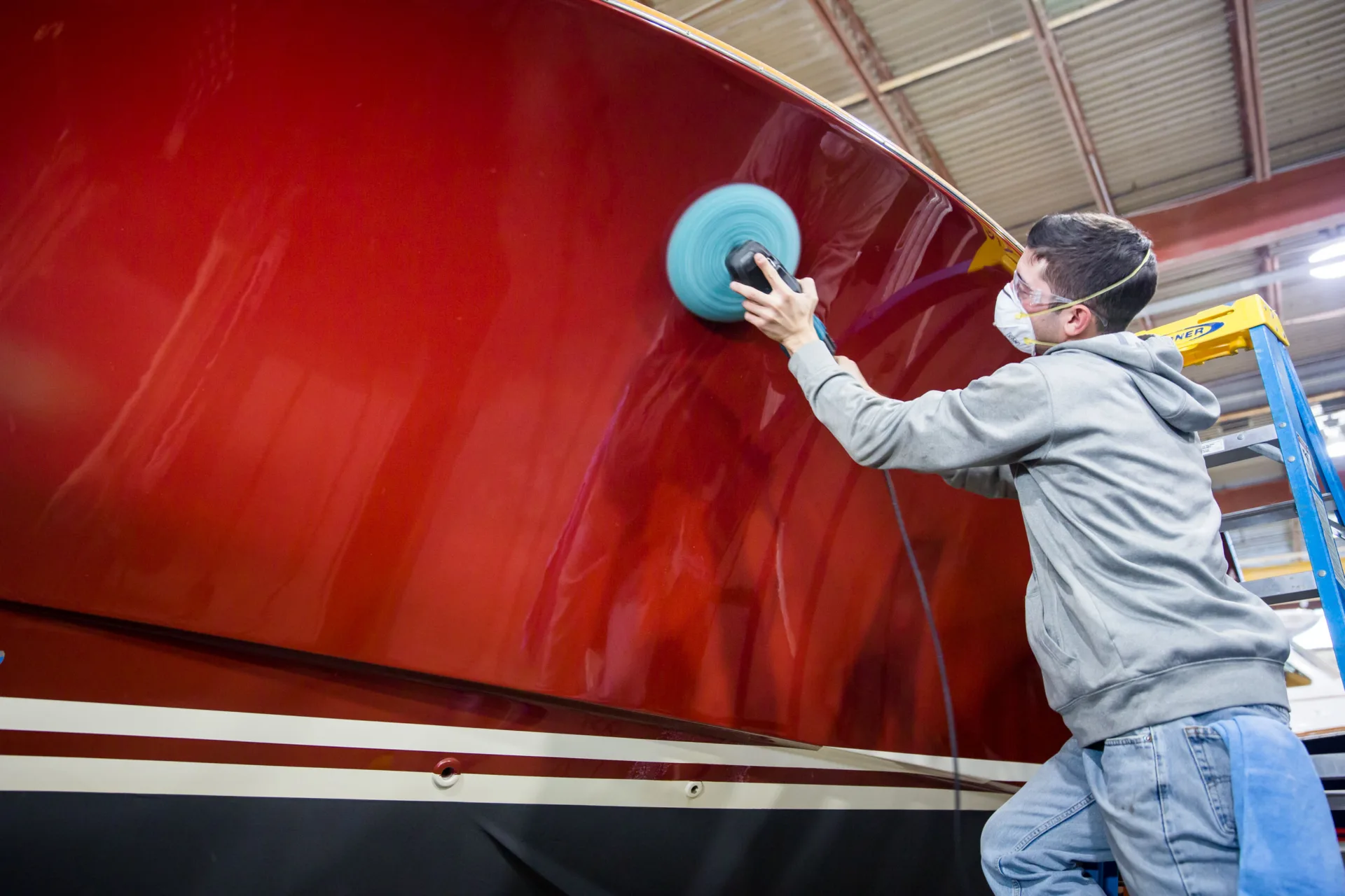 Technician polishing a yacht hull inside the service yard.