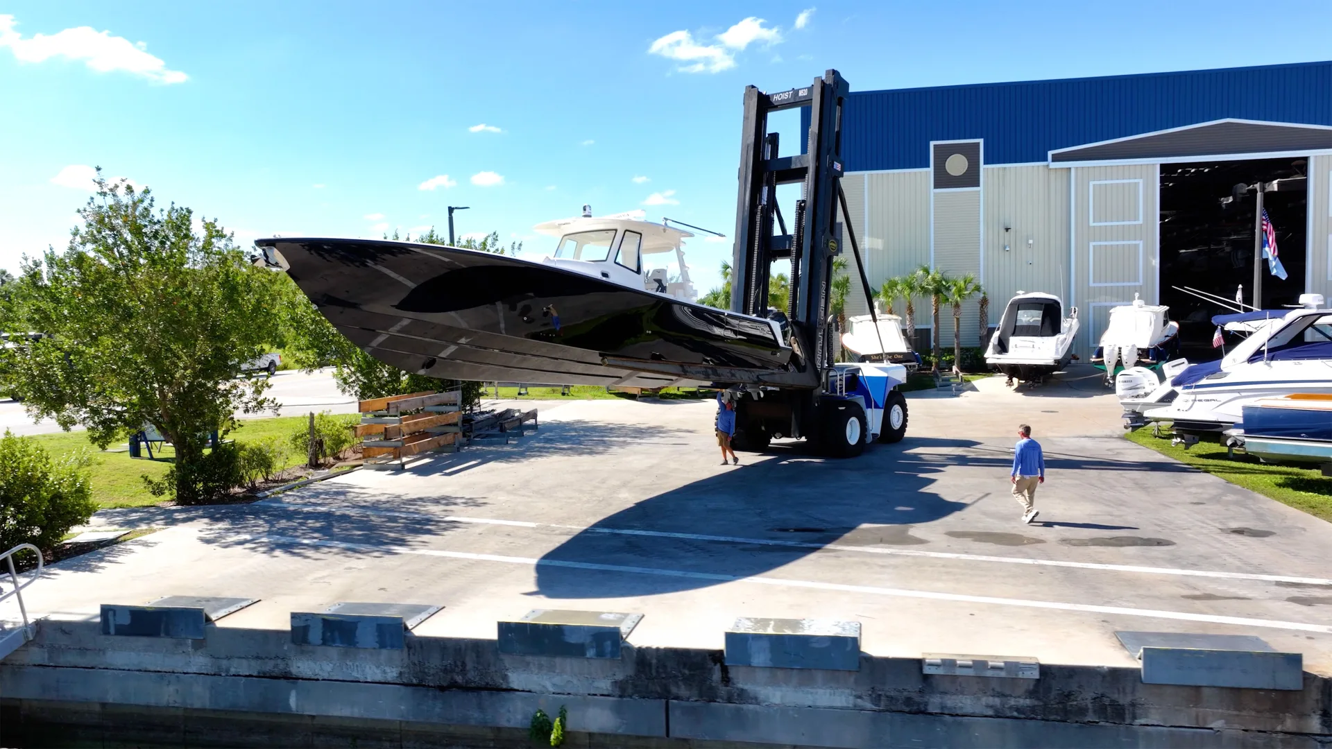 Forklift hauling a covered boat beside the Fort Myers service building