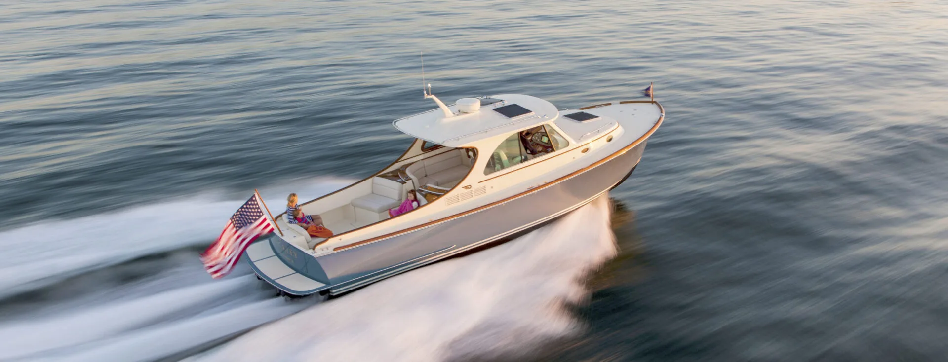 Hinckley motor yacht cruising at high speed on open water with American flag at sunset