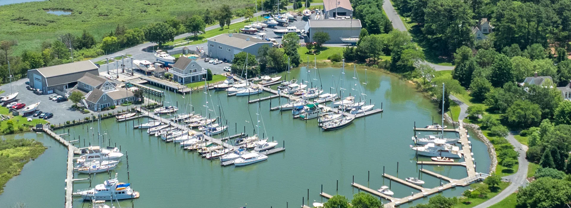 Aerial view of Hinckley Yachts’ waterfront boatyard and marina at Bachelor Point, showing docks, sailboats, and the Chesapeake Bay shoreline surrounded by green landscape.